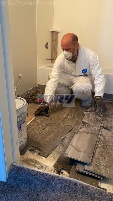technician performing emergency restoration services by removing water damaged laminate flooring in a bathroom. - iDry Columbus